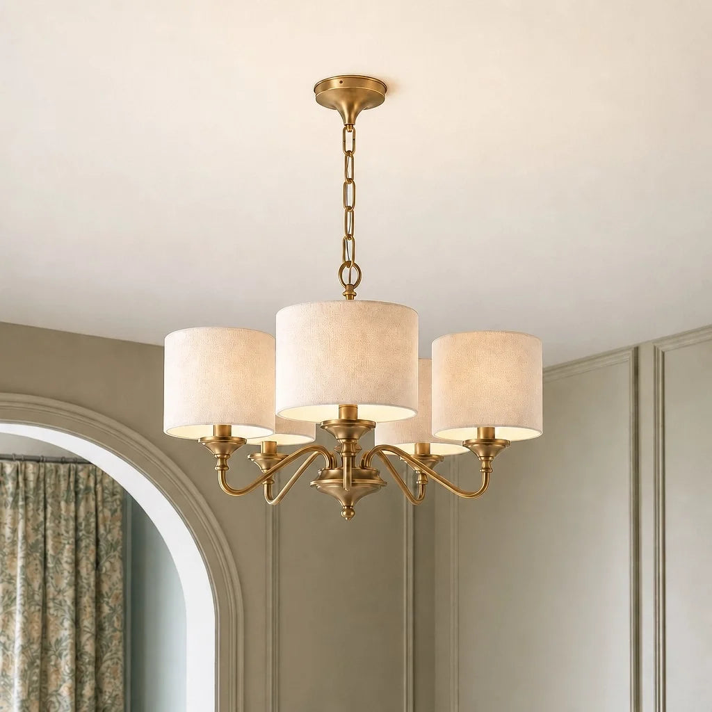 Gold chandelier with white lampshades hanging in a room with a mirror and curtain.